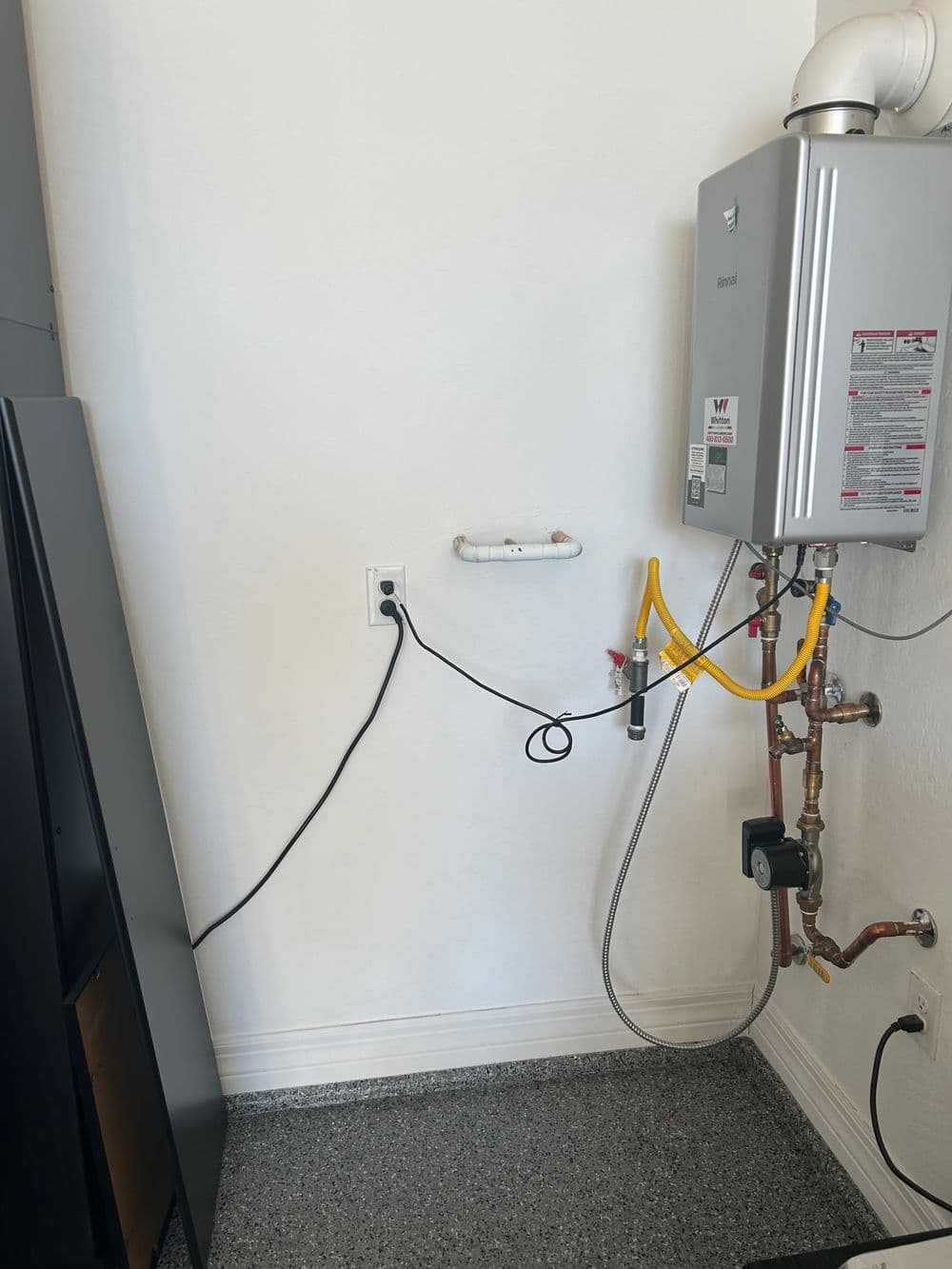 Tankless water heater installation in a home utility room, with connected pipes and electrical outlets.