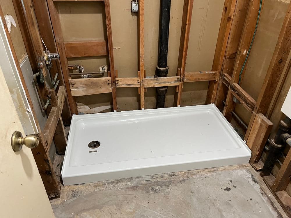 Renovated shower area with a white shower base and exposed framing and plumbing.