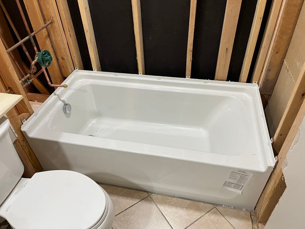 Newly installed white bathtub in a partially renovated bathroom with exposed framing.
