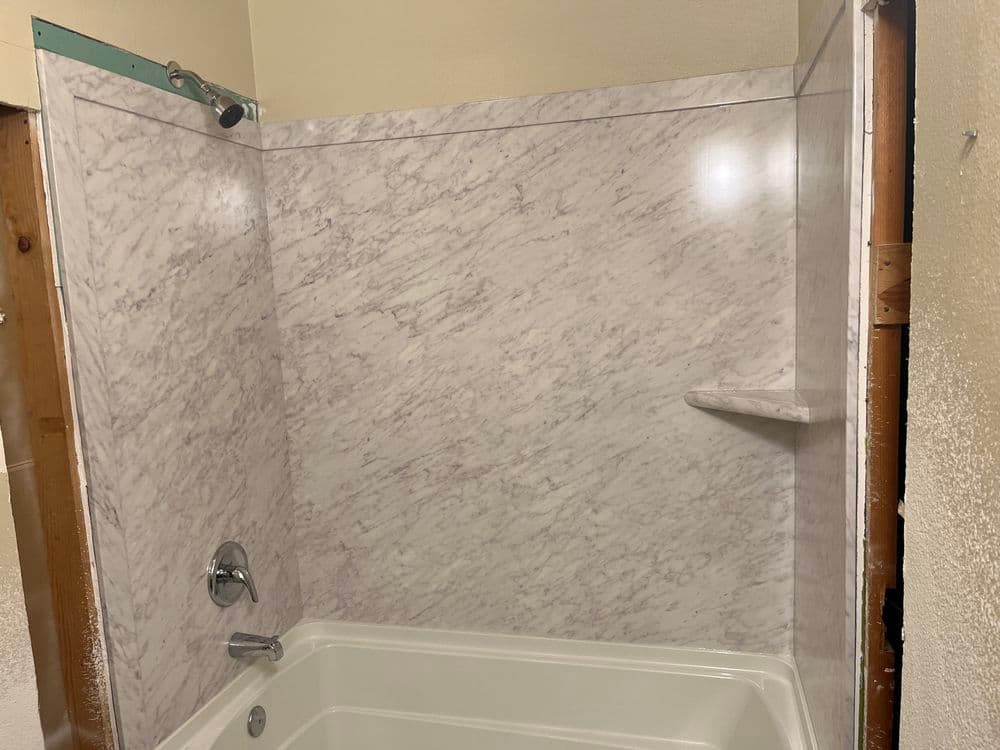 Modern bathroom with a marble-patterned shower wall and a white bathtub.