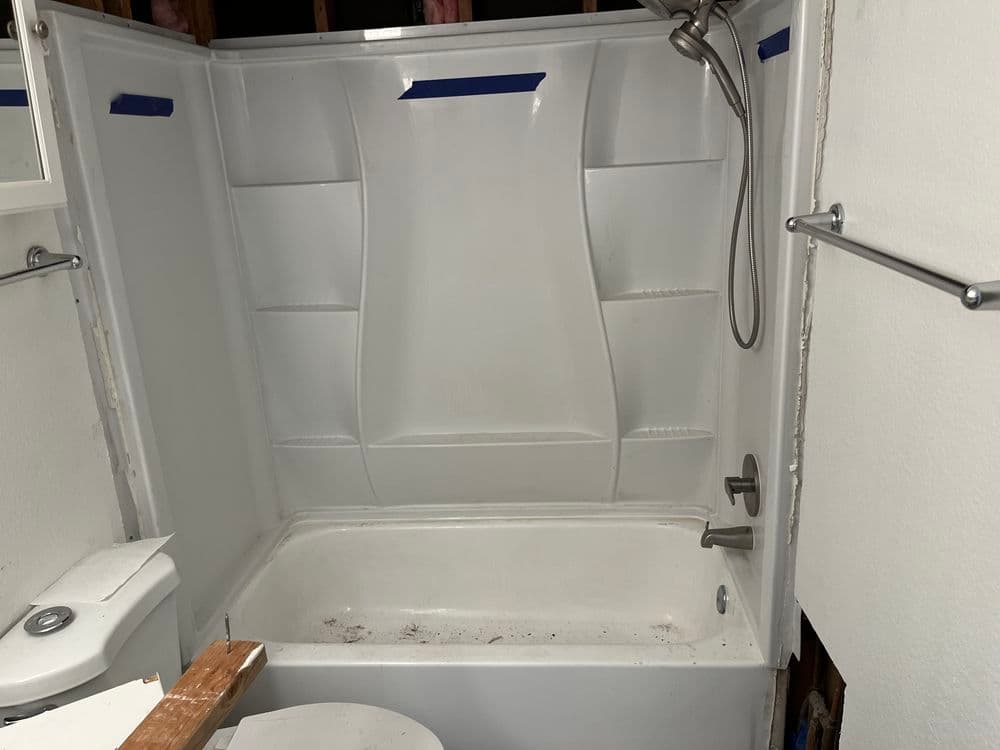 Renovated bathroom shower and bathtub area with unfinished walls and tools.