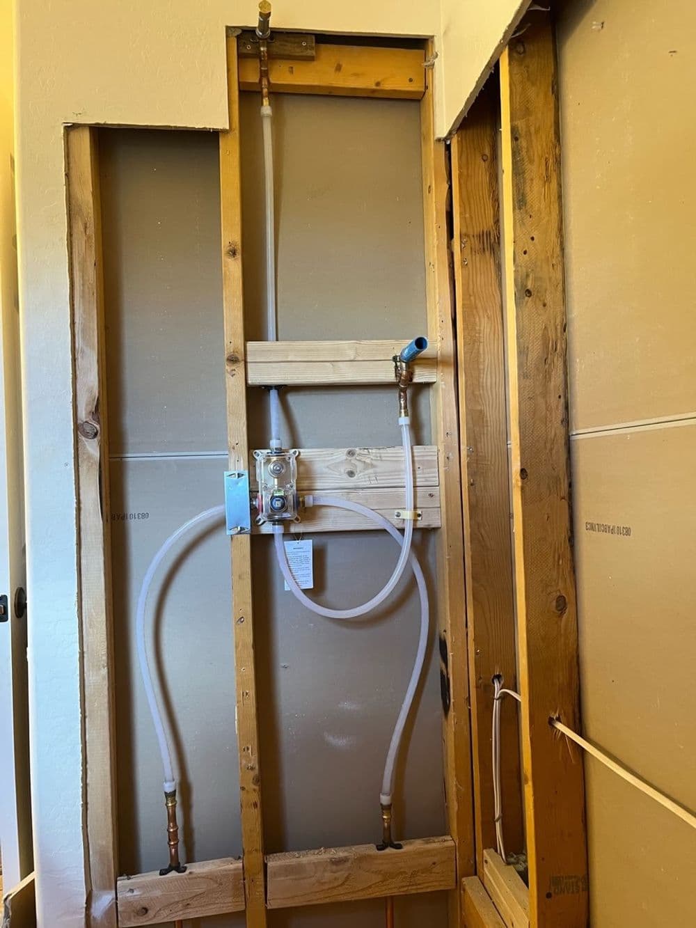 Plumbing installation with pipes and a valve within wooden wall frames.