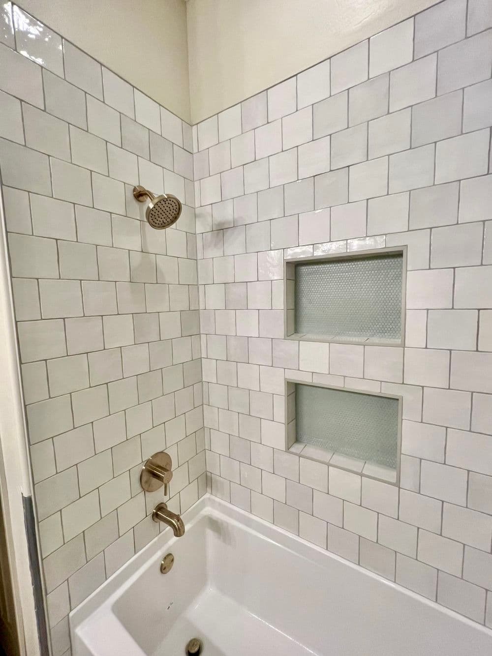 Modern bathroom featuring white subway tile, a showerhead, and dual nooks for toiletries.