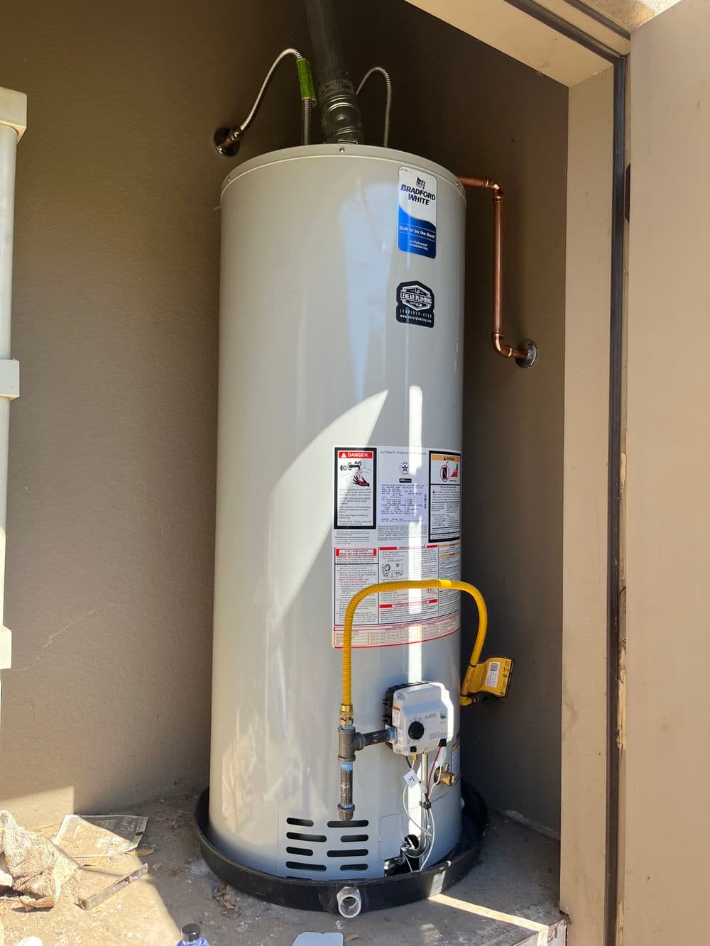 New water heater installation in a corner with plumbing and safety labels visible.