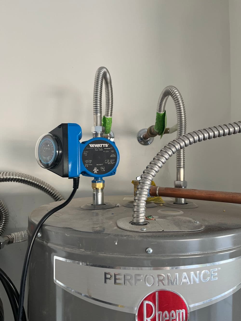 Blue water gauge on a silver Rheem water heater with connected pipes and fittings.