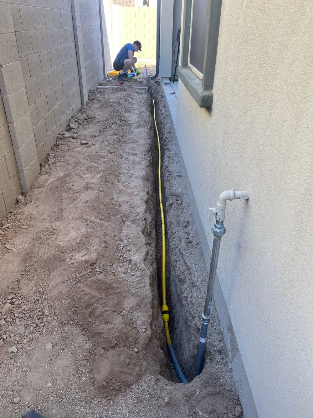 Construction worker digging a trench for utility installation next to a house.