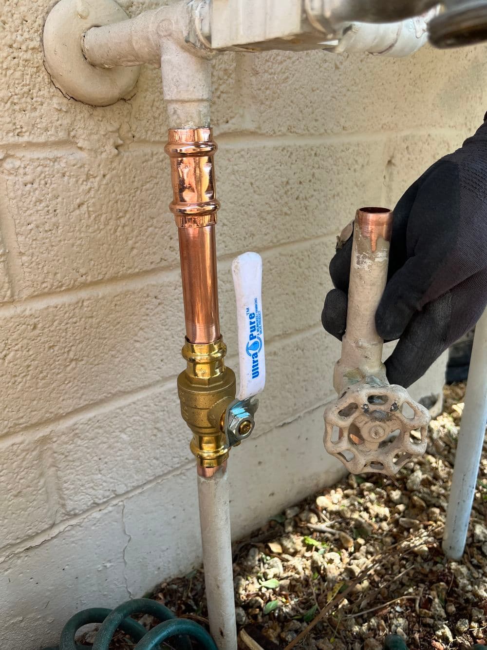 Copper plumbing valve installation with hand holding a valve near a wall.