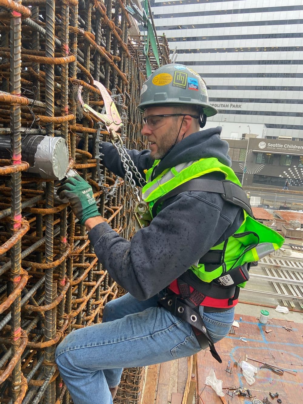 Construction worker securing rebar with safety gear on a high-rise site in rainy weather.