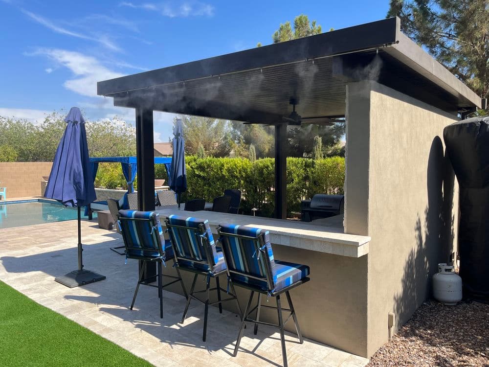 Outdoor bar with four blue chairs, pool in the background, under a shaded patio.