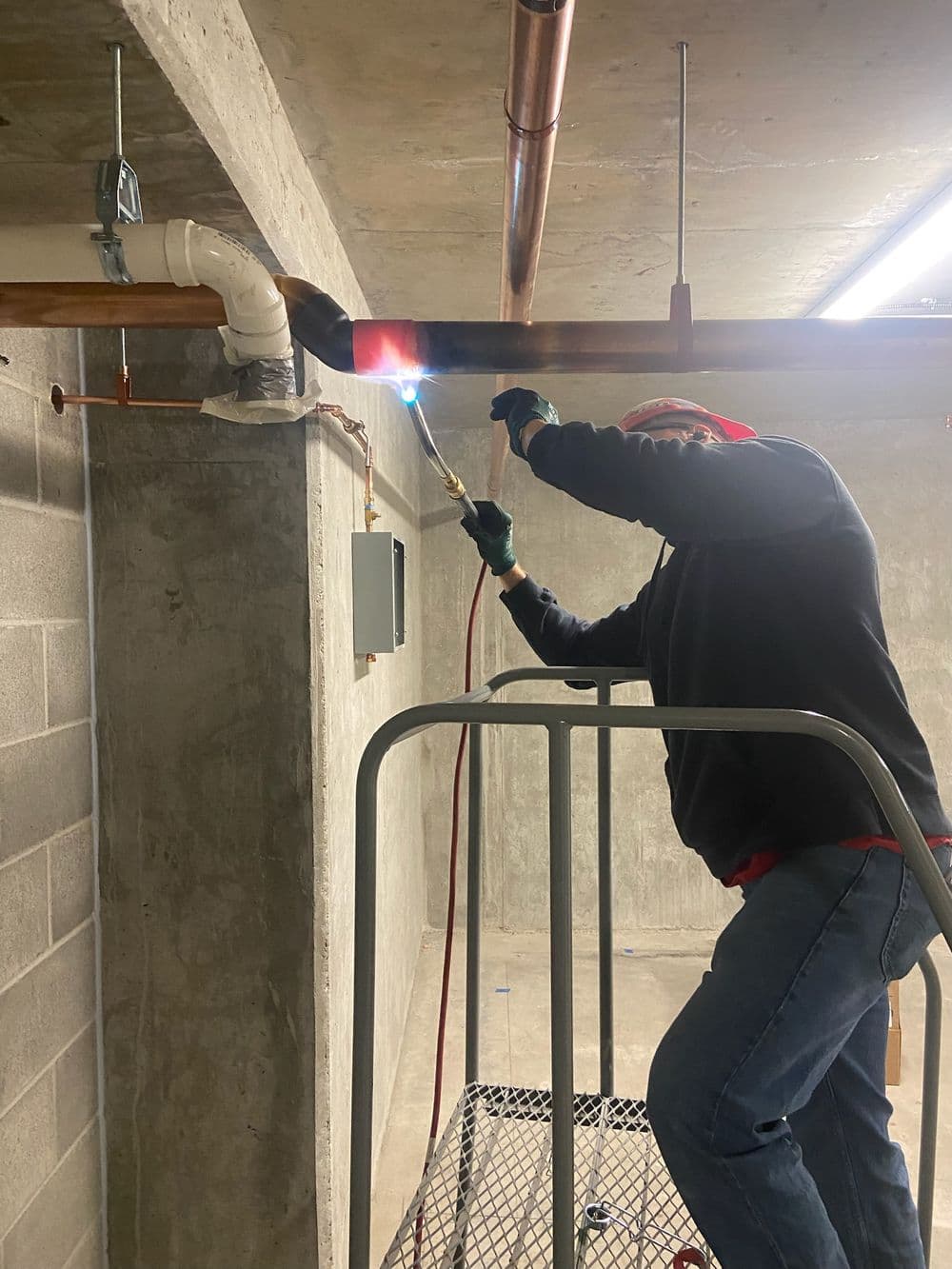 Worker using a torch to solder pipes on a scaffold in a construction site.
