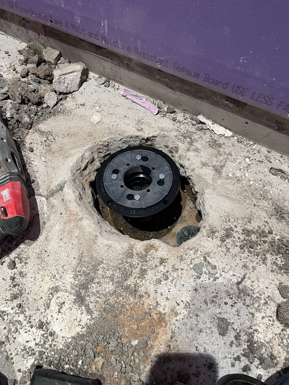 Black floor flange installed in concrete slab, with surrounding debris and tools visible.