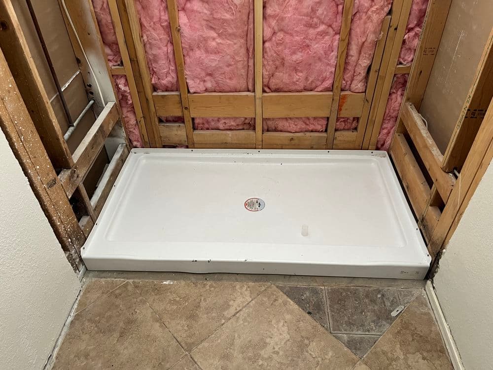 Shower base installation in a partially constructed bathroom with exposed framing.