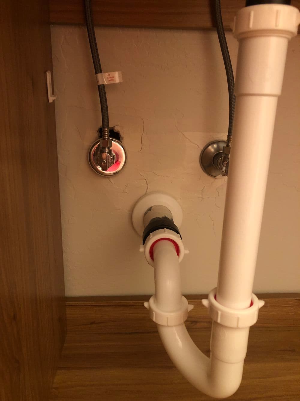 Under-sink plumbing setup featuring water supply lines and a drain pipe.