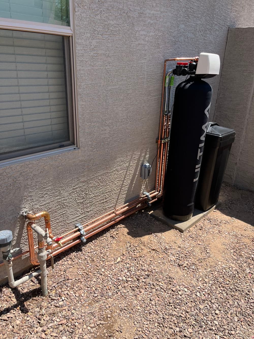 Residential water filtration system with copper piping and black storage tank near window.