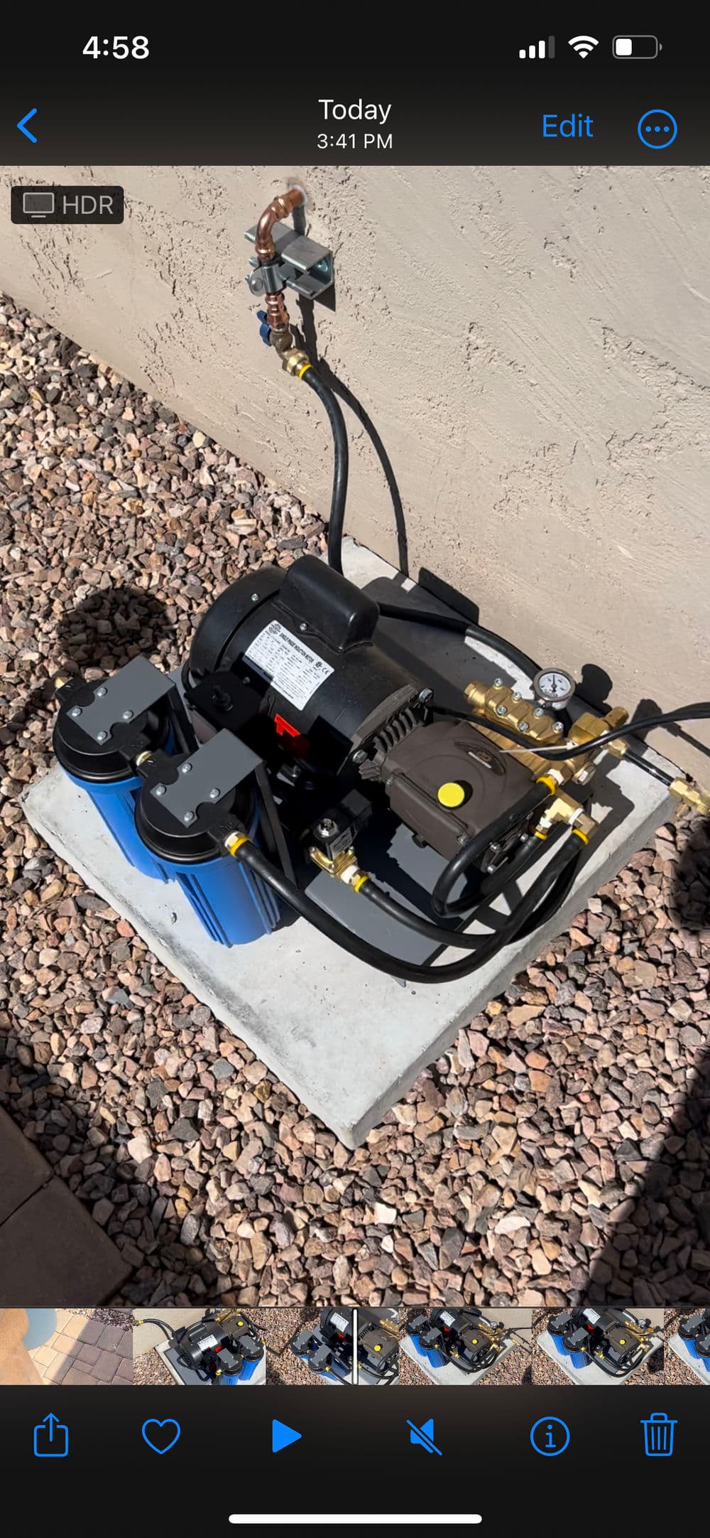 Air compressor on a concrete slab, featuring pressure gauge and hoses, surrounded by gravel.