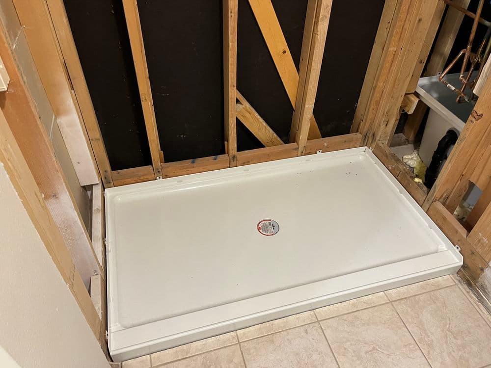 Shower base installed in partially constructed bathroom, exposed framing visible.