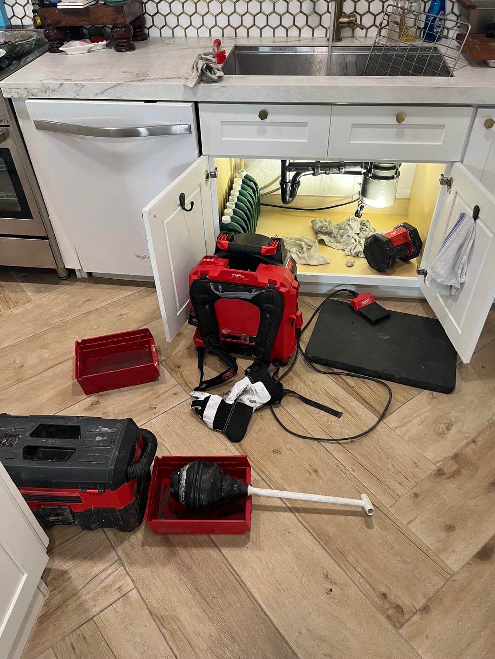 Tools and equipment scattered under kitchen sink during plumbing repair.