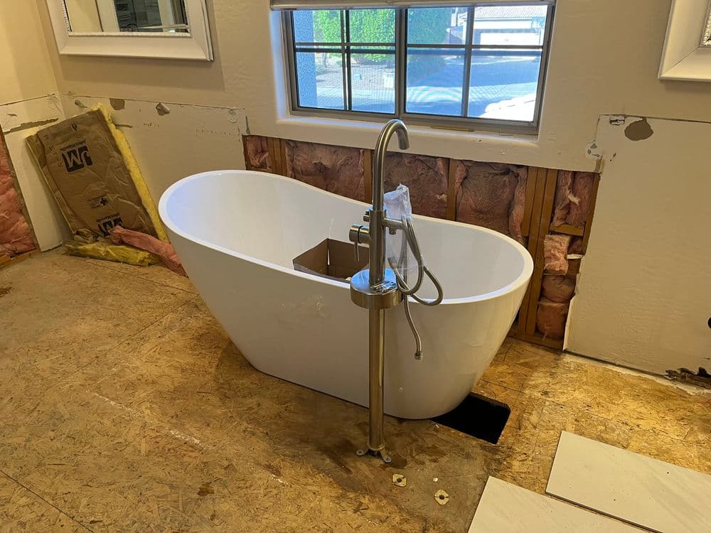 Modern freestanding bathtub with a sleek faucet in an unfinished bathroom setting.
