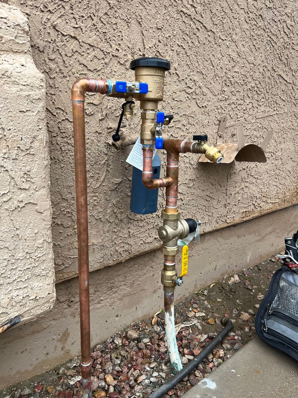 Copper plumbing installation with water meter and pressure regulator on exterior wall.