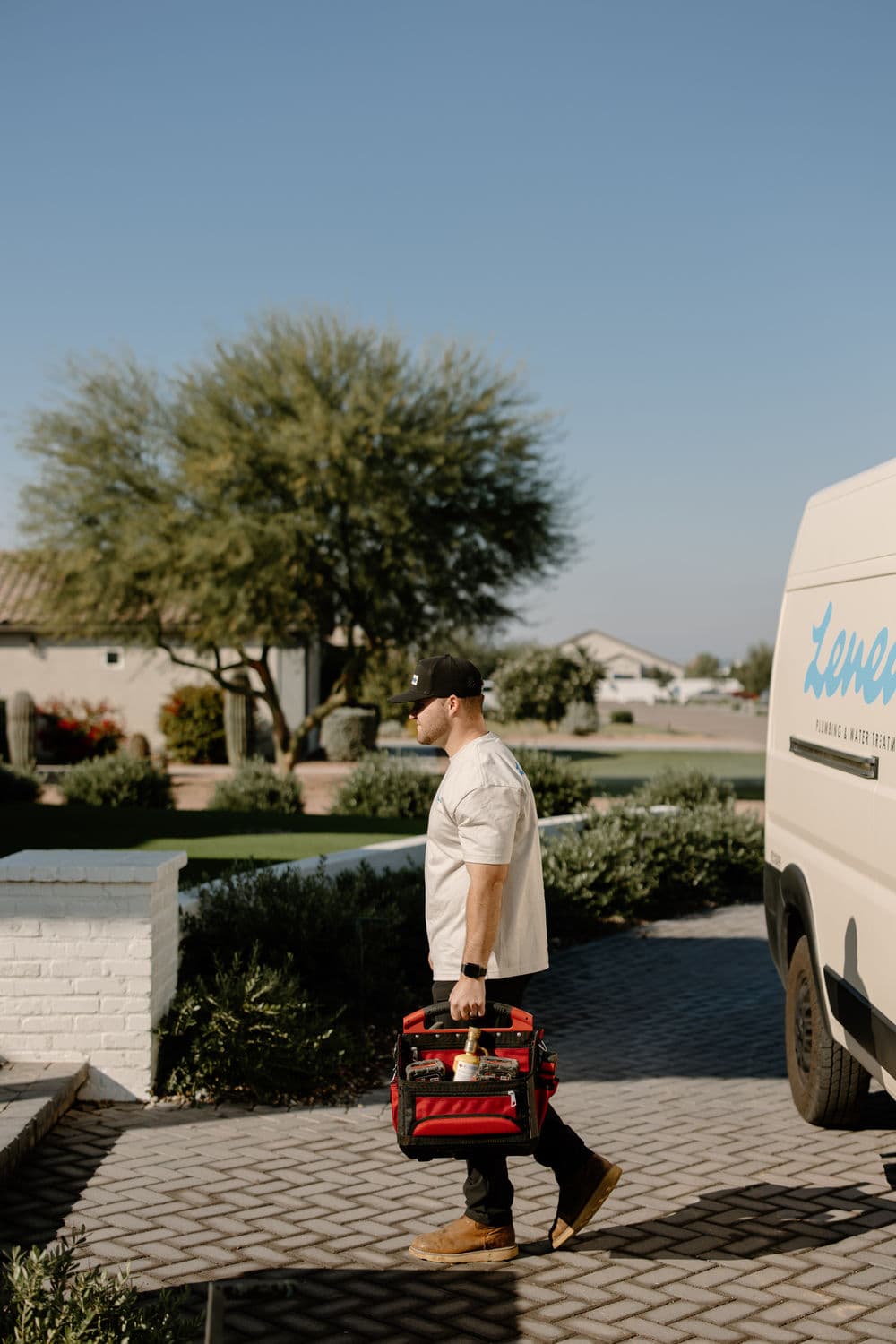 Plumber carrying tools near work van in a sunny residential neighborhood.