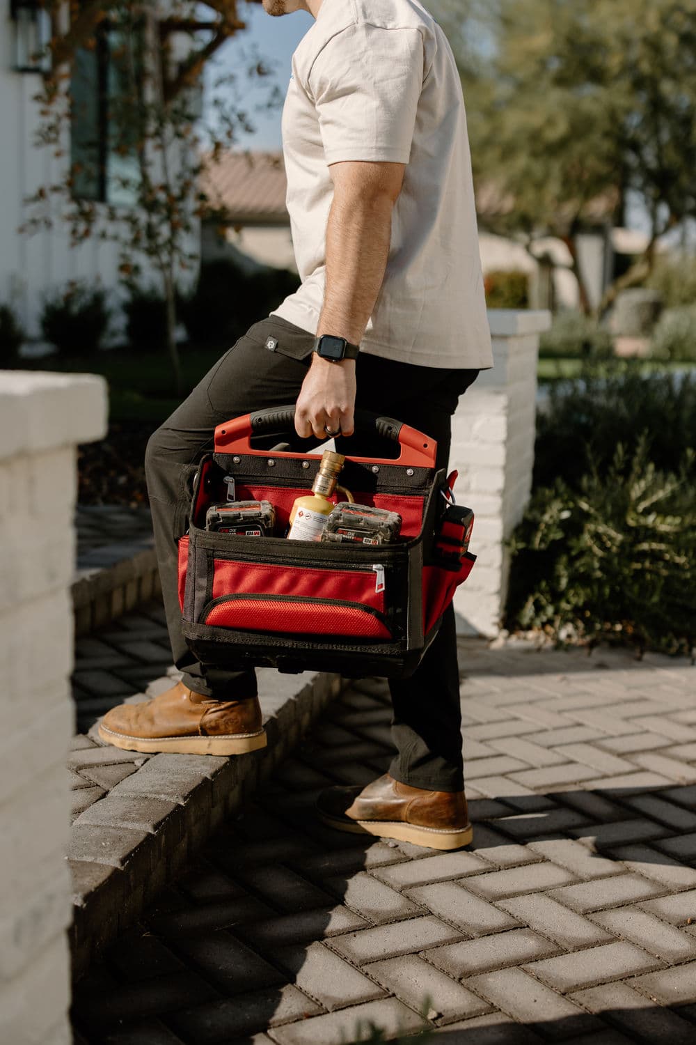Person carrying a red tool bag up stairs, wearing casual attire and a smartwatch.